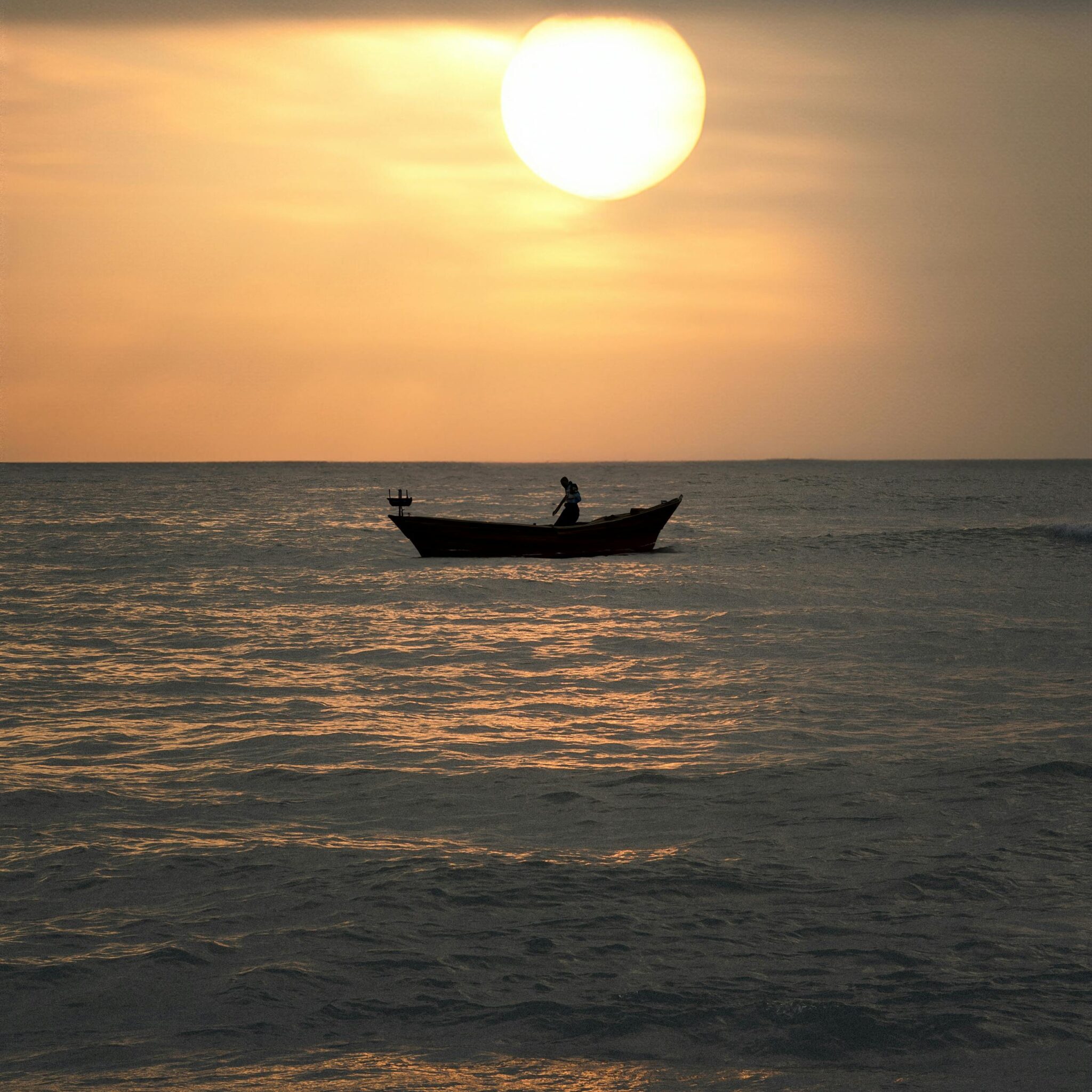 A tranquil boat ride at sunset in Kanyakumari, India, with a silhouette against the sunlit sea.