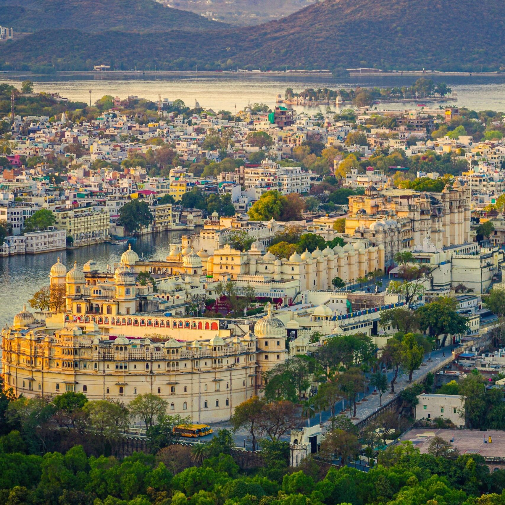 Aerial view of the historic Udaipur City Palace and surrounding cityscape against a tranquil lake backdrop.