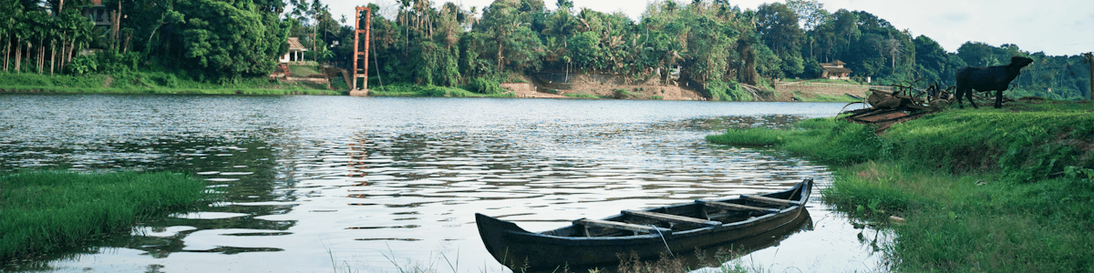 Tranquil riverside scene featuring a traditional boat and lush greenery in Ramamangalam, Kerala.